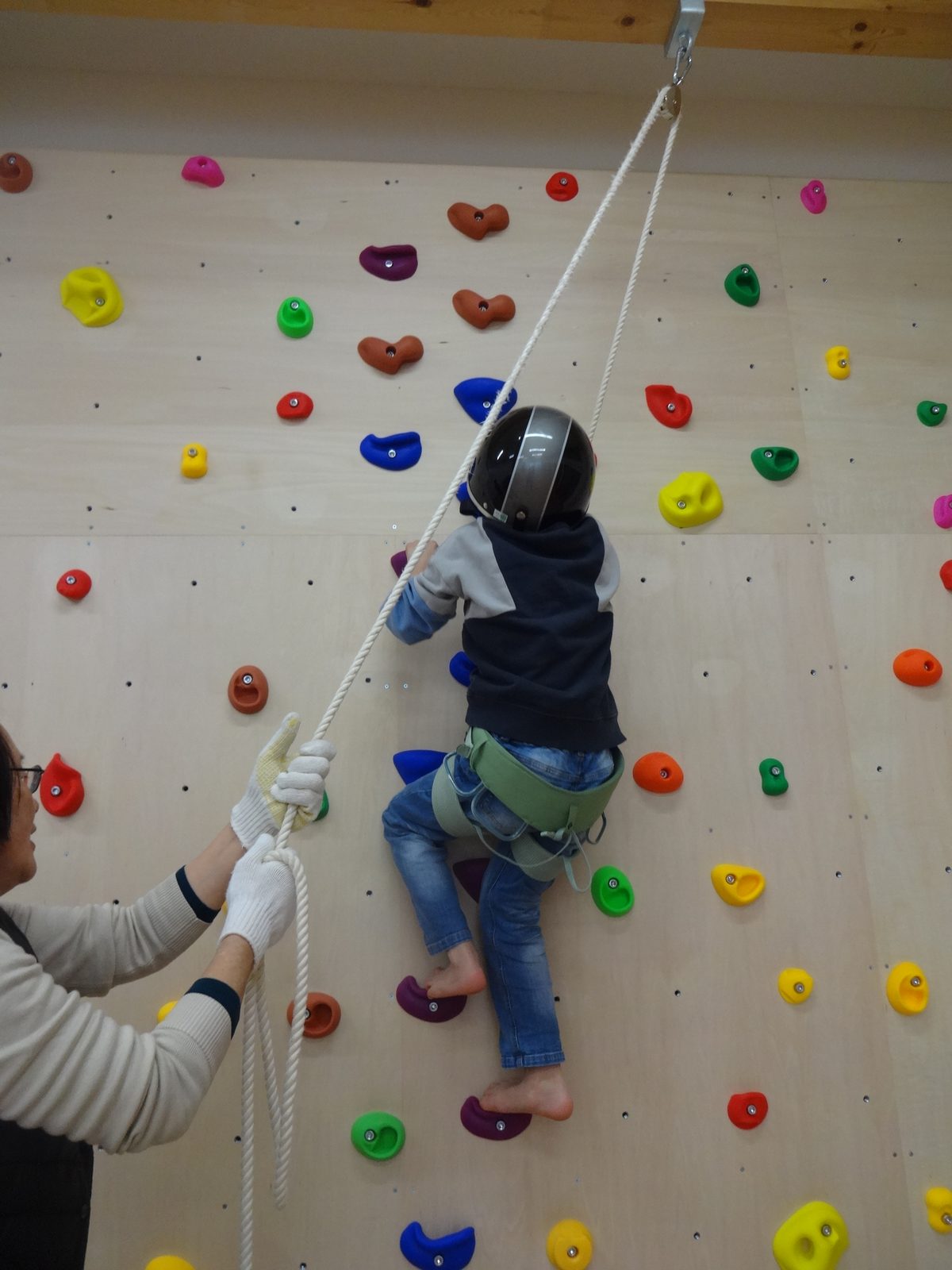クライミングウォールに挑戦する子どもと、ロープで支えるスタッフ
