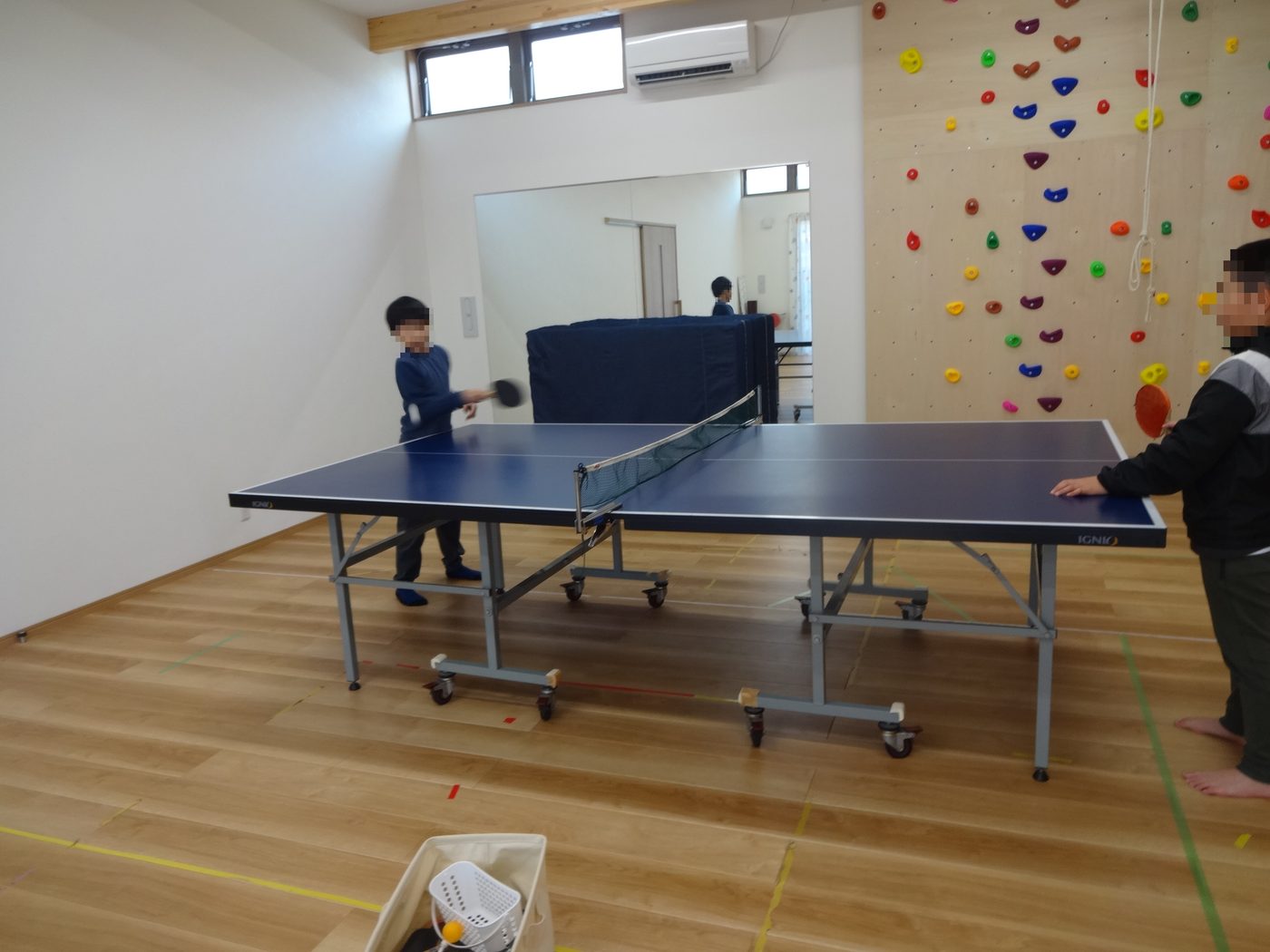 クライミングウォールのあるプレイルームで卓球をする子どもたち